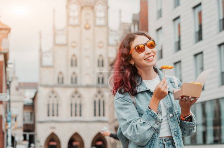 Foto de Alegre chica feliz merienda en comida rápida con camarones en masa o papas fritas en la calle de la ciudad de Munster en Alemania en una caja de papel para llevar - Imagen libre de derechos