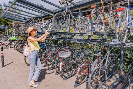 Photo for 30 July 2022, Cologne, Germany: Cyclist girl at the two-storey intercept parking for bicycles near the city transport hub. Safe Storage and bicycle infrastructure in a modern city - Royalty Free Image