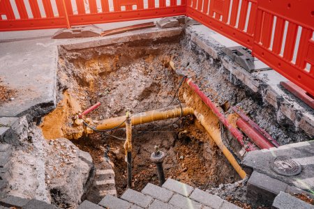 Excavation on a city street to replace plastic water pipes or laying cables. Repair and renovation at construction and development site. Fence for safety of pedestrians and cars.