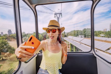 Photo for A travel blogger girl takes a selfie photo on a smartphone in a cable car with a view of the city of Cologne - Royalty Free Image