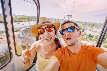 Photo for A couple of travel blogger girl and guy takes a selfie photo in a cable car with a view of the city of Cologne - Royalty Free Image