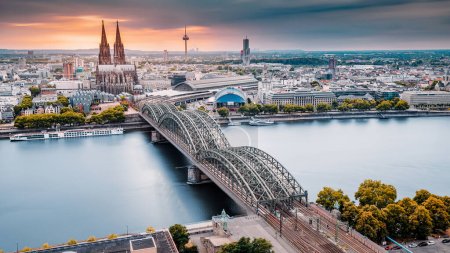 Téléchargez les photos : Cologne Vue aérienne avec des trains se déplacent sur un pont au-dessus du Rhin sur lequel circulent des barges et des navires à passagers. Majestueuse cathédrale de Cologne en arrière-plan - en image libre de droit