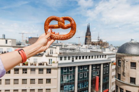 tourist hand with a traditional pretzel snack on the background of an Cologne cathedral building. Travel and tourism in Germany and Rhineland