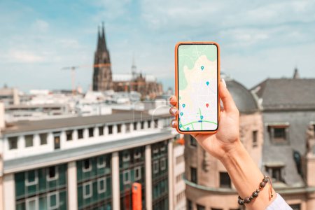 Foto de Una chica turística con un teléfono inteligente en la pantalla de los cuales es una aplicación con mapas y geolocalización en las calles de la vieja ciudad europea. Catedral de Colonia en el fondo - Imagen libre de derechos