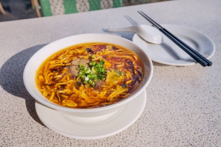 Heiß-saure chinesische oder taiwanesische Suppe mit frischen Zutaten auf einem Teller im Restaurant mit Essstäbchen. Traditionelle asiatische Küche und Gerichte