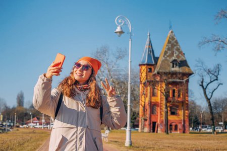 Tourist girl taking selfie photos on her smartphone against Towers on Palic lake, while travelling in Serbia