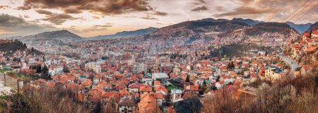 panorama of Sarajevo as the sun sets behind its rolling hills, casting a colorful hue over the cityscape.