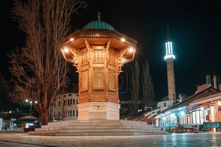 historische Straßen des Sarajevo-Viertels Bascarsija bei Nacht, wo der beleuchtete Sebilj-Brunnen als zeitloses Wahrzeichen islamischer Architektur steht.