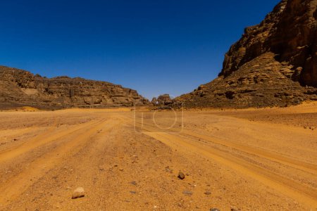 Photo for Empty sandy dirt road with tire tracks in Tassili National Park. Tadrart mountains, Acacus range. Tassili N'Ajjer National Park. Algeria, Africa - Royalty Free Image