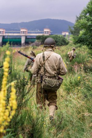 Historical reconstruction. World War II infantry division soldiers patrol a site in the tall grass. View from the back.  Porbka, Poland