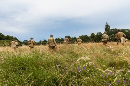 Photo for Historical reconstruction. World War II american infantry  soldiers  patrol the area  in the tall grass. View from the back.  Porbka, Poland - Royalty Free Image