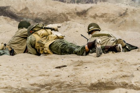 Téléchargez les photos : Soldats américains combattant sur la plage lors de la reconstruction de la bataille historique avec la Seconde Guerre mondiale. Vue de l'arrière. Hel, Pologne - en image libre de droit