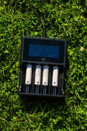 Foto de Cargador de batería AA negro con baterías alcalinas recargables en el césped. La batería se está cargando. - Imagen libre de derechos