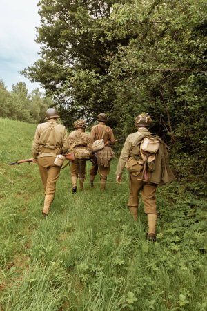 Téléchargez les photos : Reeneactors historiques habillés en soldat d'infanterie américain pendant la Seconde Guerre mondiale patrouiller la forêt. Vue de l'arrière. Porbka, Pologne - en image libre de droit