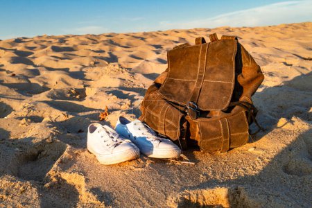 Téléchargez les photos : Concept de voyage et vacances. Baskets blanches et élégant sac à dos marron sur une plage de sable. Mer Baltique, Hel, Poméranie, Pologne - en image libre de droit