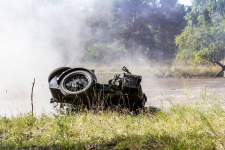 Téléchargez les photos : Reconstruction historique. Une moto allemande renversée et sale entre fumée et poussière après une explosion de bombe.. - en image libre de droit