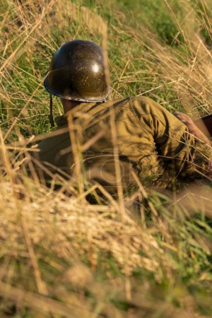 Foto de Reconstrucción histórica. Un soldado de infantería estadounidense de la Segunda Guerra Mundial se prepara para atacar escondido en la hierba alta. Vista desde atrás - Imagen libre de derechos