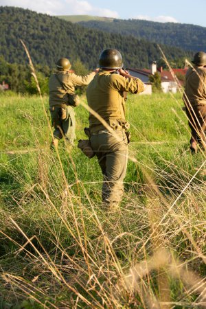 Photo for Historical reenactment. American  soldiers during the Second World War.  Infantry soldiers patrol the area ready to fire. View from the back. - Royalty Free Image
