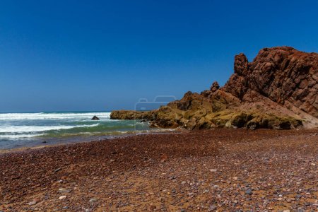 Foto de Pintorescas rocas rojas costeras en la costa del Océano Atlántico.Playa de Legzira (mineral Gzira). Marruecos, África. - Imagen libre de derechos