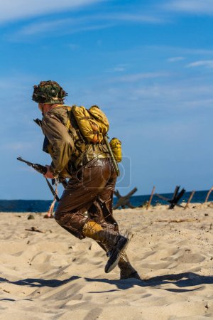 Historical reconstruction. An American infantry soldier from the World War II  fighting on the beach. Wet soldier runs on beach. 
