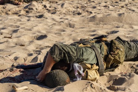 Historical reconstruction. Injured or dead World War II infantry  soldier  on the beach. View from the back. 
