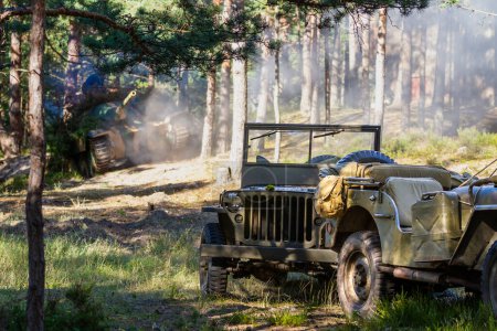 Historical reenactment. Two abandoned US military vehicles stand in the forest on the battlefield in dust and smoke after a shell explosion.