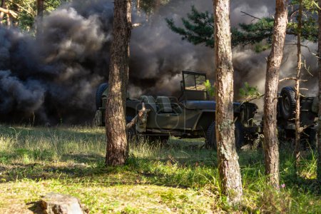 Historische Nachstellung. Zwei verlassene US-Militärfahrzeuge stehen nach einer Granatenexplosion im Wald auf dem Schlachtfeld in Staub und Rauch.