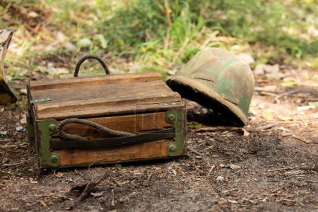 De cerca. Vieja caja de municiones militares alemanas de madera en el suelo. En el fondo un casco Wehrmacht m35 en cubierta de camuflaje