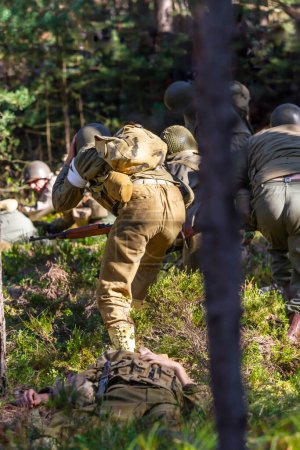 Historical reconstruction. American  infantry soldiers during the Second World War fighting in the forest. View from the back.