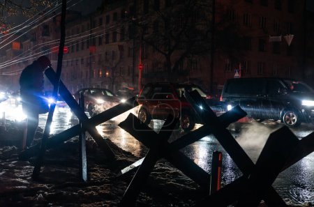 Téléchargez les photos : KYIV, UKRAINE - 16 décembre 2022 : Bâtiments sombres sans lumière lors d'une panne d'électricité à Kiev. Des hérissons antichars sont visibles dans les phares des voitures. - en image libre de droit