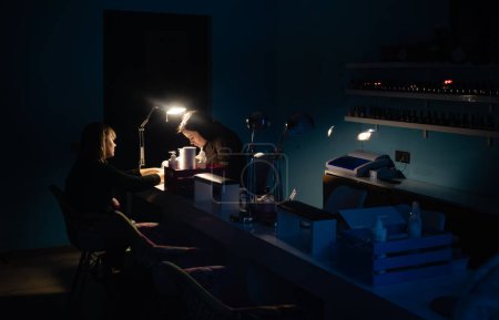 Photo for KYIV, UKRAINE - Dec. 14, 2022: Nail salon in Kyiv during the blackout. A manicurist is seen working with a client in the light of emergency lamps. - Royalty Free Image