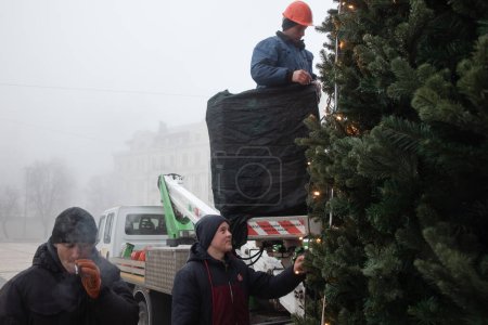 Téléchargez les photos : KYIV, UKRAINE - 17 décembre 2022 : Des travailleurs des services publics installent et décorent un sapin de Noël sur la place Sofiyivska à Kiev par une journée brumeuse - en image libre de droit