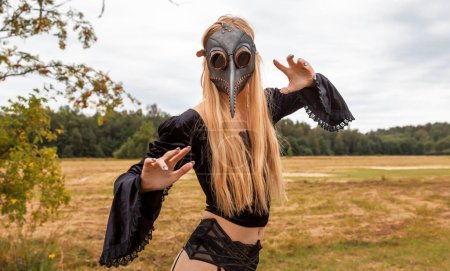 Photo for A fascinating and surreal photo of a woman in a crow mask amidst a field and forest. - Royalty Free Image