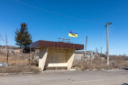 Téléchargez les photos : Un arrêt de bus avec des traces de débris provenant des bombardements et un drapeau ukrainien comme symbole du peuple ukrainien invincible. Bogorodichne, région de Donetsk, Ukraine - en image libre de droit