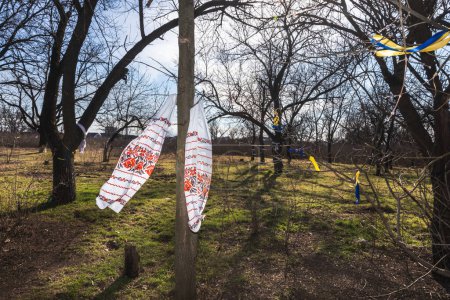 Téléchargez les photos : Serviette nationale ukrainienne sur les branches d'arbres en l'honneur des héros de la Défense territoriale morts le 01 mars 2022 dans le parc Lilas à Kherson. - en image libre de droit