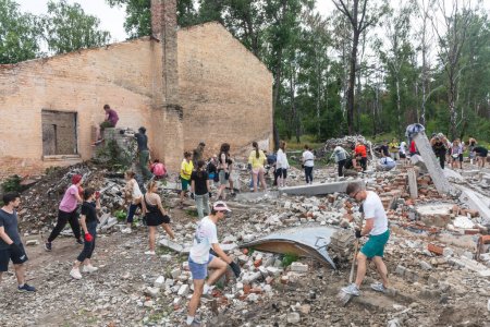 Téléchargez les photos : YAHIDNE, UKRAINE - 8 JUILLET : Les bénévoles de l'organisation "Repair Together" sont débarrassés des décombres d'une maison de culture locale endommagée par la guerre, nettoyant et empilant les briques pour les réutiliser. - en image libre de droit