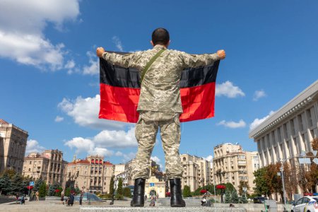 Téléchargez les photos : KYIV, UKRAINE - 24 août 2023 : Un homme en uniforme militaire tient le drapeau de l'Organisation des nationalistes ukrainiens lors d'une exposition de matériel militaire russe détruit - en image libre de droit