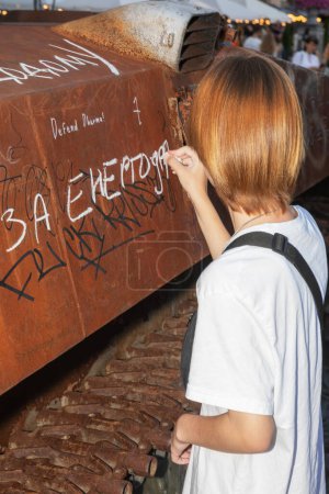 Téléchargez les photos : KYIV, UKRAINE - 24 août 2023 : Une fille écrit sur l'armure de l'inscription du réservoir brûlé For Energodar. - en image libre de droit