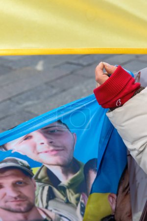 Foto de KYIV, UCRANIA - 10 de diciembre de 2023: Manifestación por la libertad de Azov en apoyo de los prisioneros de guerra ucranianos. Un retrato de un héroe prisionero de guerra se ve impreso en la bandera de Ucrania - Imagen libre de derechos