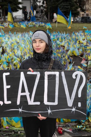 Téléchargez les photos : KYIV, UKRAINE - 18 février 2024 : Une jeune femme tient une affiche AZOV GRATUITE sur fond d'un grand nombre de drapeaux ukrainiens avec les noms des prisonniers et des morts - en image libre de droit
