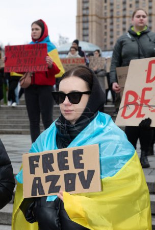 Téléchargez les photos : KYIV, UKRAINE - 18 février 2024 : Une jeune femme est vue avec le drapeau de l'Ukraine sur les épaules tenant une affiche AZOV GRATUIT. - en image libre de droit