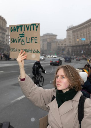 Photo for KYIV, UKRAINE - Feb. 18, 2024: A young woman with a placard "Captivity Does Not Equal Saving Life" is seen during the action in support of prisoners of war FREE AZOV - Royalty Free Image
