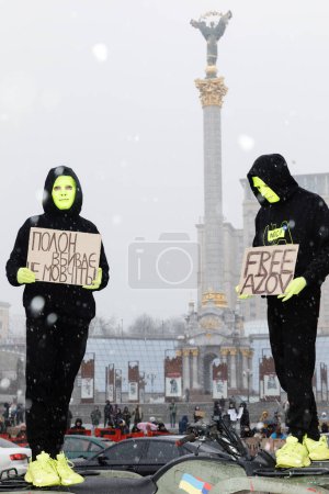 Photo for KYIV, UKRAINE - Feb. 18, 2024: Two figures in masks with placards "Free Azov" and "Don't be silent - captivity kills" are seen in the background of the Independence Monument of Ukraine. - Royalty Free Image