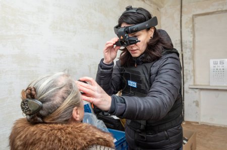 Téléchargez les photos : CHASIV YAR, DONETSK REG., UKRAINE - mars 2024 : Une ophtalmologiste de la mission Frida Ukraine examine une femme âgée à l'aide d'un équipement médical mobile de pointe - en image libre de droit