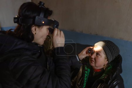 Téléchargez les photos : SIVERSK, DONETSK REG., UKRAINE - mars 2024 : Une ophtalmologiste de la mission bénévole Frida Ukraine examine la vision d'une femme âgée dans un refuge souterrain - en image libre de droit