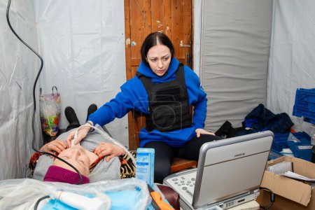 Téléchargez les photos : SIVERSK, DONETSK REG., UKRAINE - mars 2024 : Une femme médecin échographe de la Frida Ukraine Volunteer Mission est vue en train de fournir une échographie à une résidente locale. - en image libre de droit