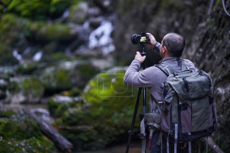 Nature photographer shooting landscapes in a canyon covered in moss and luxuriant vegetation, with a river