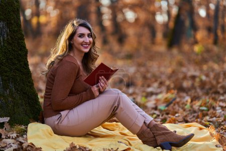 Téléchargez les photos : Jeune femme lisant un livre en plein air dans la forêt à la fin de l'automne au coucher du soleil - en image libre de droit