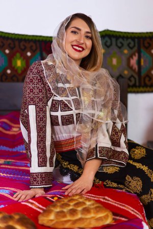 Photo for Young Romanian woman dressed up in traditional popular costume, in a traditional rural home - Royalty Free Image