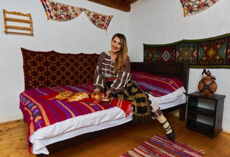 Téléchargez les photos : Jeune Roumaine vêtue d'un costume populaire traditionnel, dans une maison rurale traditionnelle - en image libre de droit